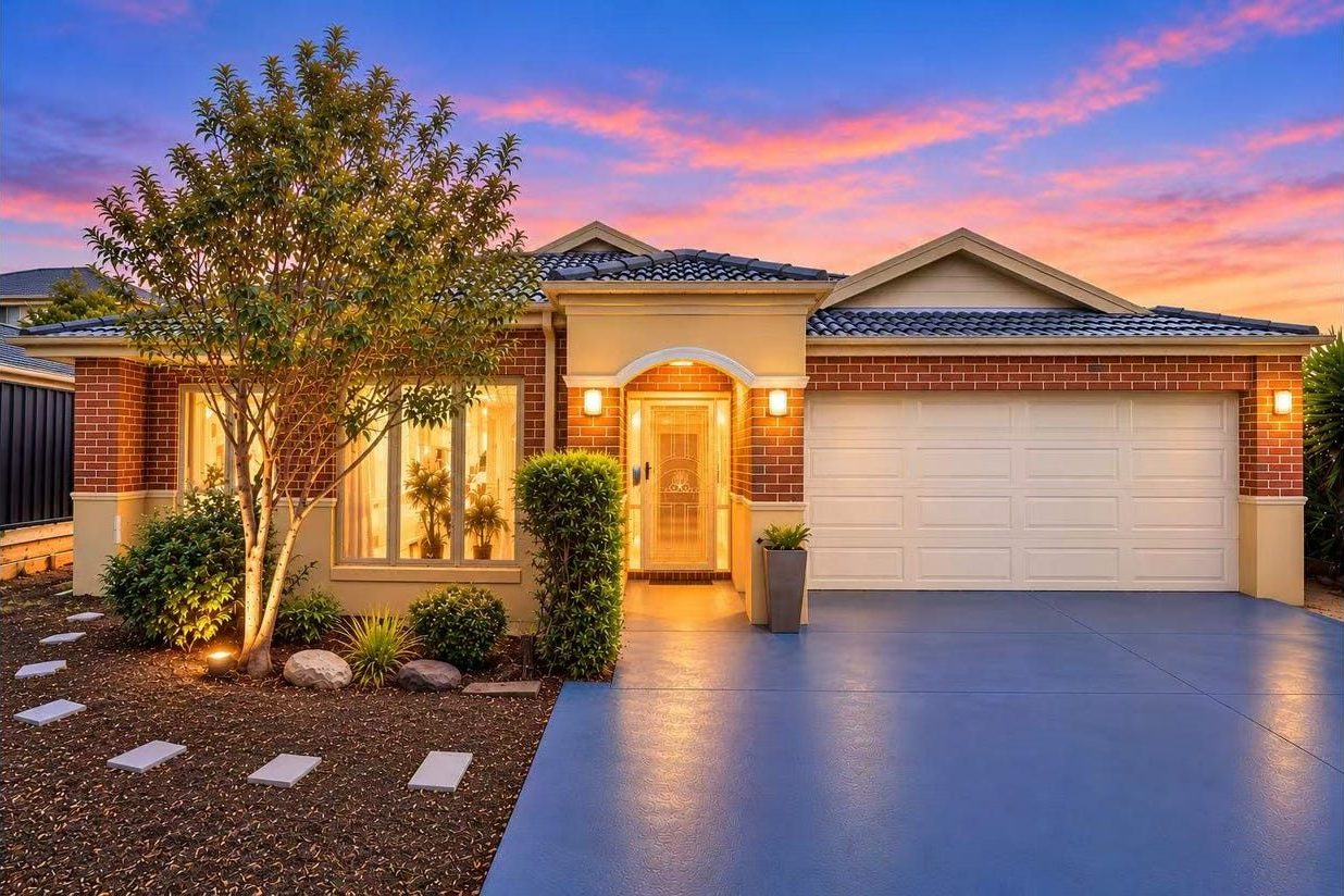 9 Gilmore Grove Point Cook — illuminated front facade at dusk with double garage, brick façade and manicured front garden